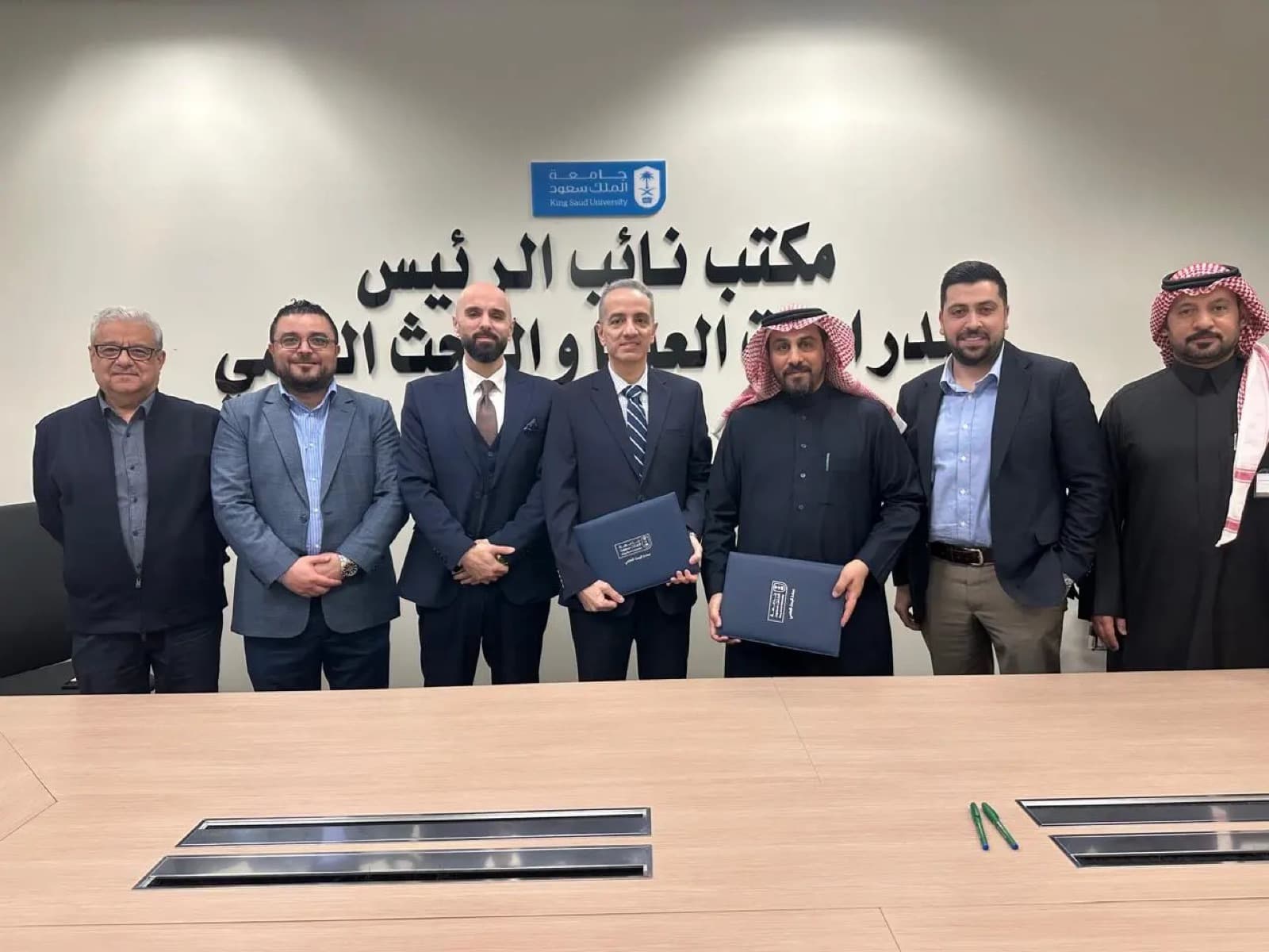 HTE Group and King Saud University representatives sign a partnership agreement around a conference table, with the King Saud University wordmark on the wall behind them.