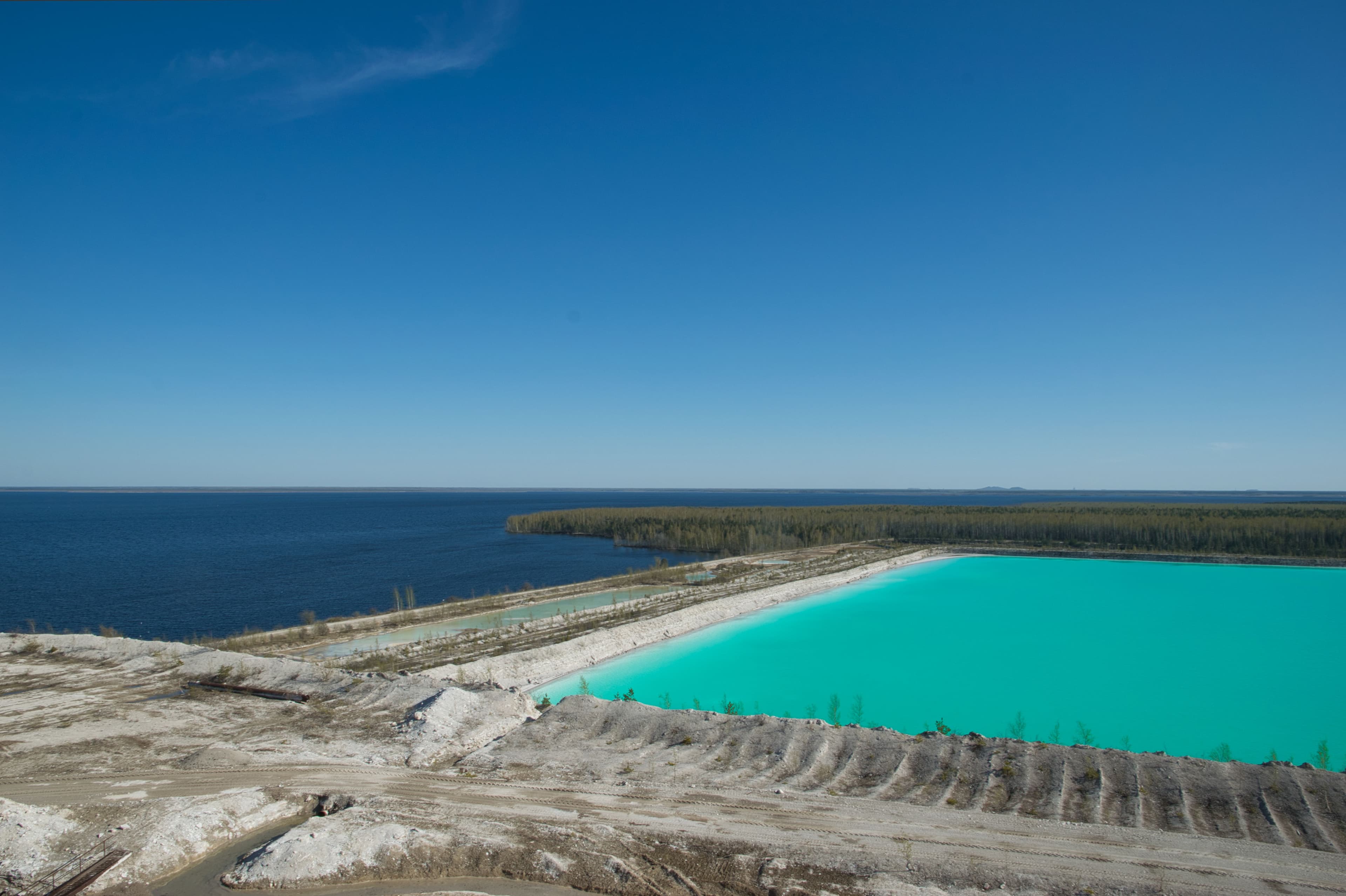 Aerial view of a turquoise engineered lagoon beside a natural lake, separated by an embankment