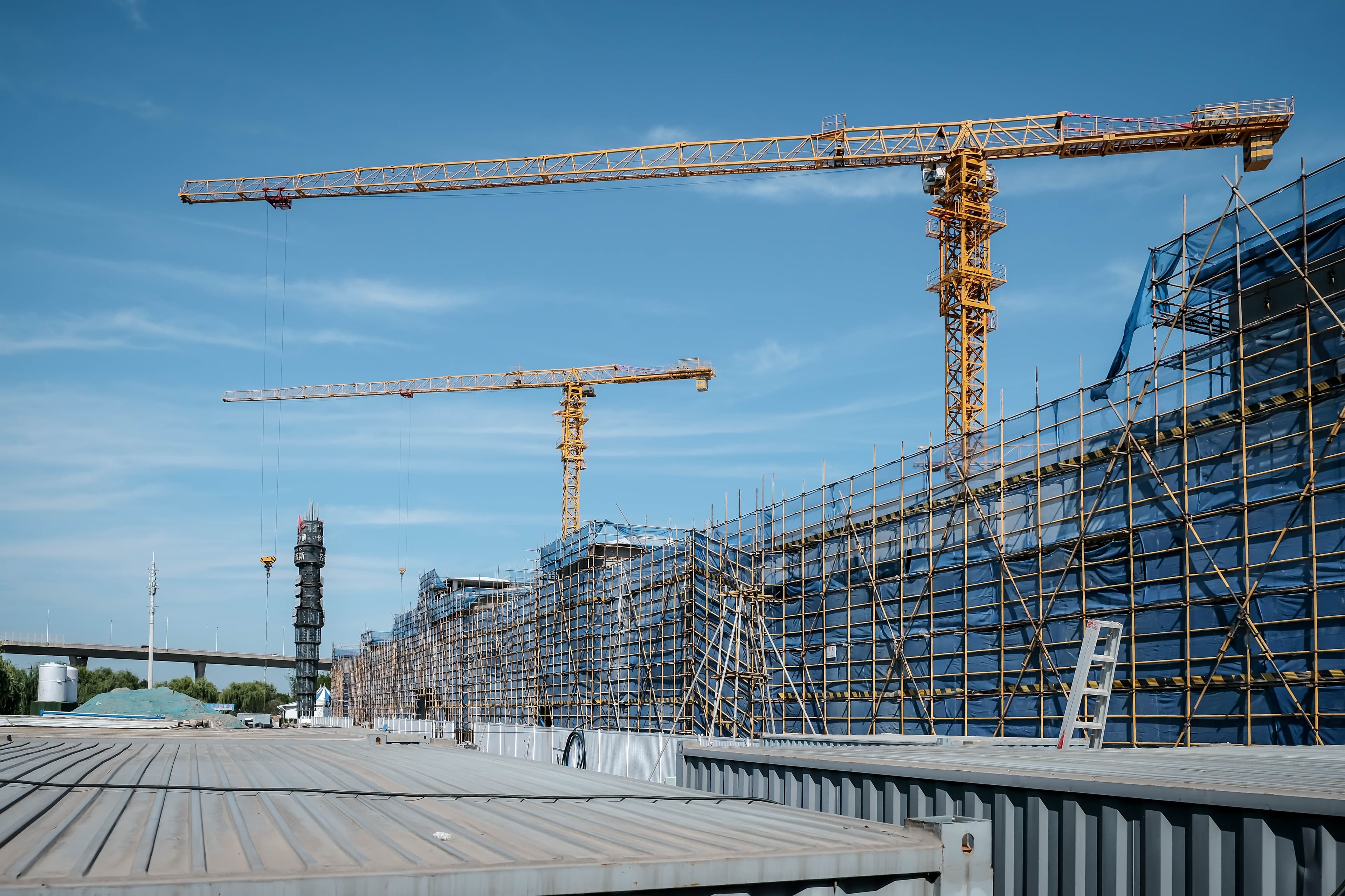 Tower cranes above a large building under construction, wrapped in scaffolding and netting