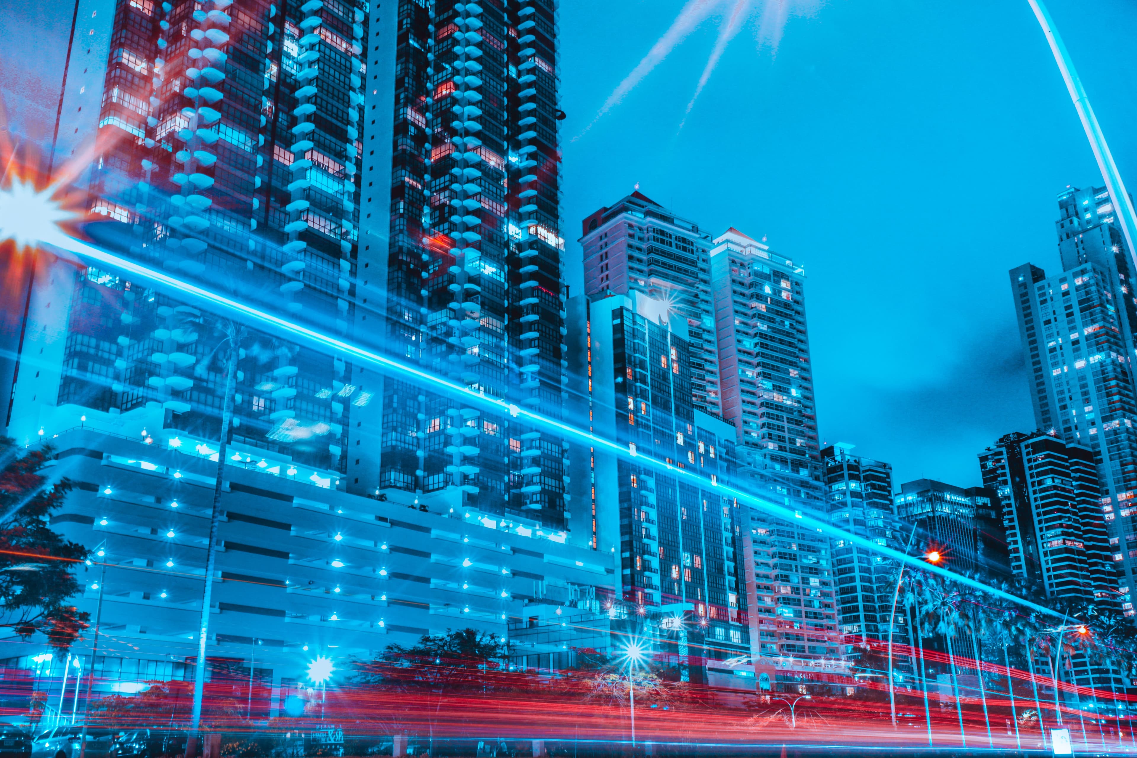 Night skyline of high-rise towers with blue and red light-trail streaks suggesting digital connectivity
