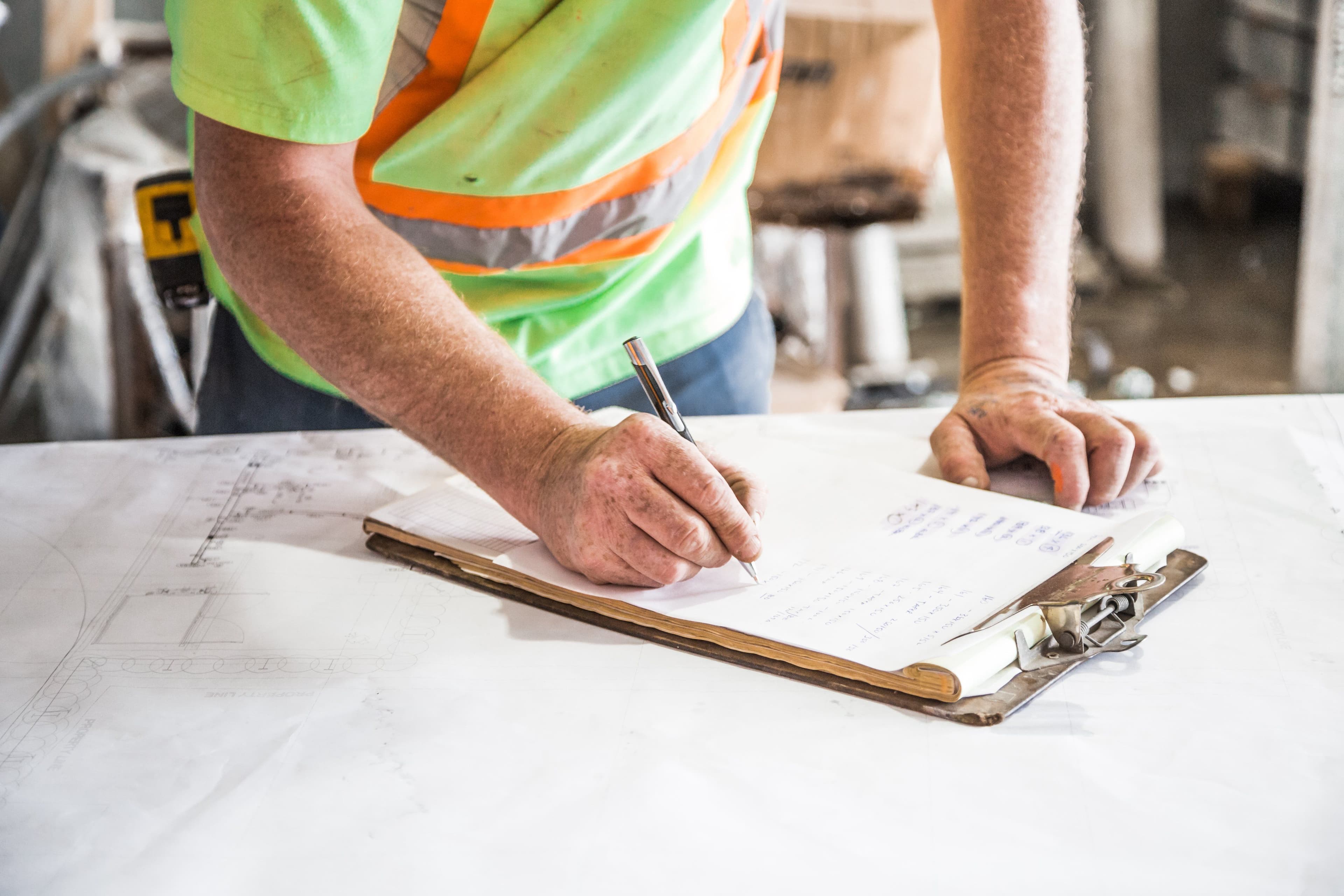 Construction worker in a hi-vis vest marking up site drawings on a clipboard