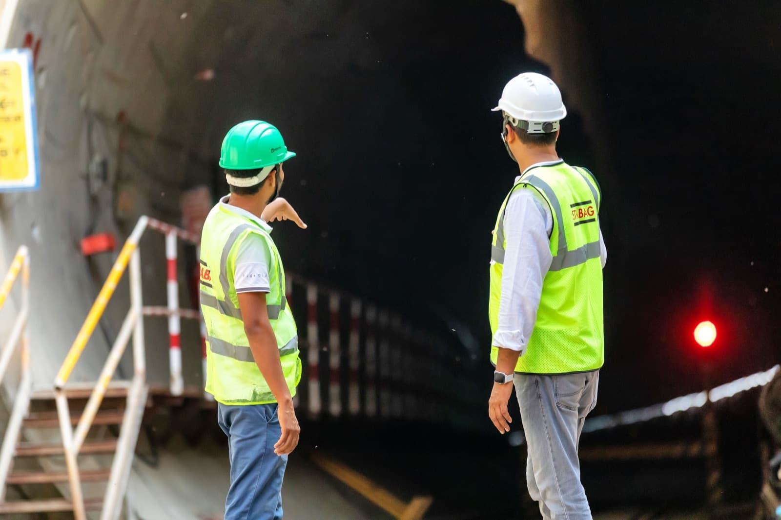 Two site supervisors in hard hats and high-visibility vests at a tunnel entrance