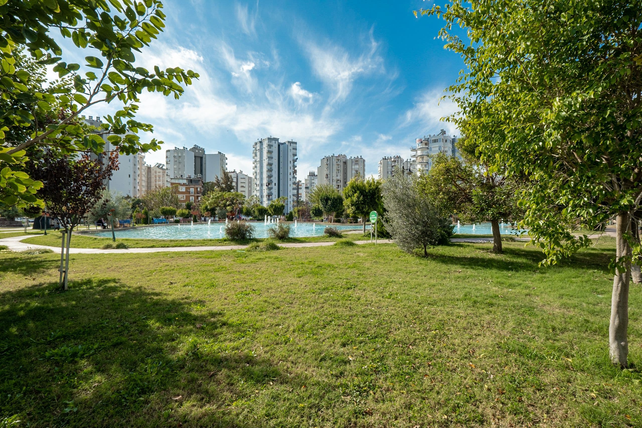 Urban park lawn with a fountain pond, trees and residential towers in the background